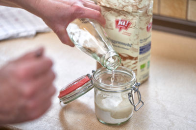 Jemand gießt Wasser in ein Glas mit Ja! Natürlich Bio-Mehl.