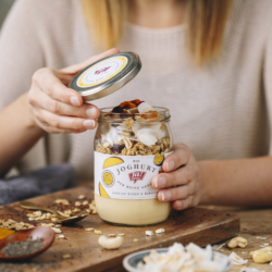 Jemand öffnet eine Ja! Natürlich Bio-Smoothie Bowl mit Granola und getrockneten Mangos.