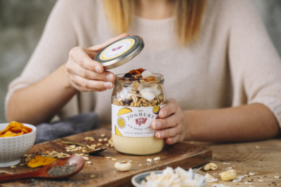 Jemand öffnet eine Ja! Natürlich Bio-Smoothie Bowl mit Granola und getrockneten Mangos.