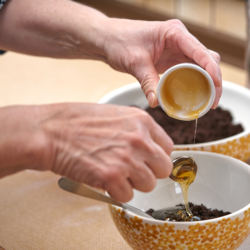 Jemand gibt einen Löffel Bio-Honig in eine Schale mit Kaffeesatz.