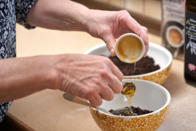 Jemand gibt einen Löffel Bio-Honig in eine Schale mit Kaffeesatz.