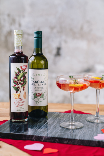 Zwei Cocktails, daneben Ja! Natürlich Bio-Weichsel-Sirup und Grüner Veltliner.