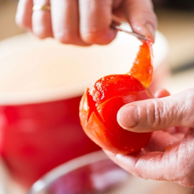 Jemand schält einen Bio-Paradeiser.