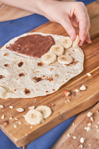 Jemand legt Bio-Bananenscheiben auf einen Wrap mit Nutella.