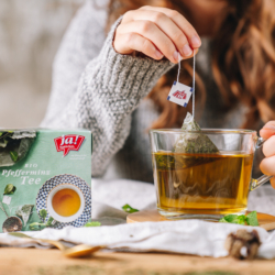 Jemand macht einen Ja! Natürlich Bio-Pfefferminztee in einer Tasse. Eine Packung des Tees steht daneben.