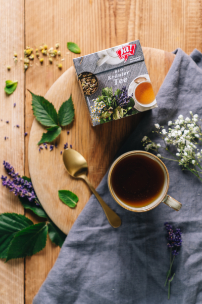 Auf einem Brett liegt eine Packung Ja! Natürlich Bio-Kräutertee und eine Tasse gefüllt mit dem Tee.