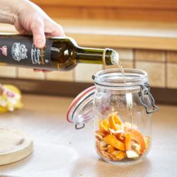 Jemand füllt Ja! Natürlich Bio-Essig in das Marmeladenglas mit Zitrusschalen.