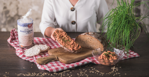 Jemand hält ein Brot mit Aufstrich, daneben steht eine Packung Ja! Natürlich Bio-Reiswaffeln.