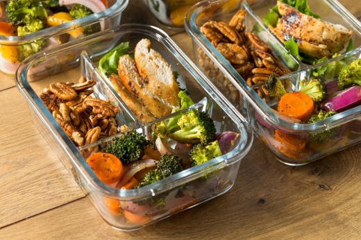 Glasbehälter mit Bio-Hähnchen und Gemüse auf einem Holztisch.