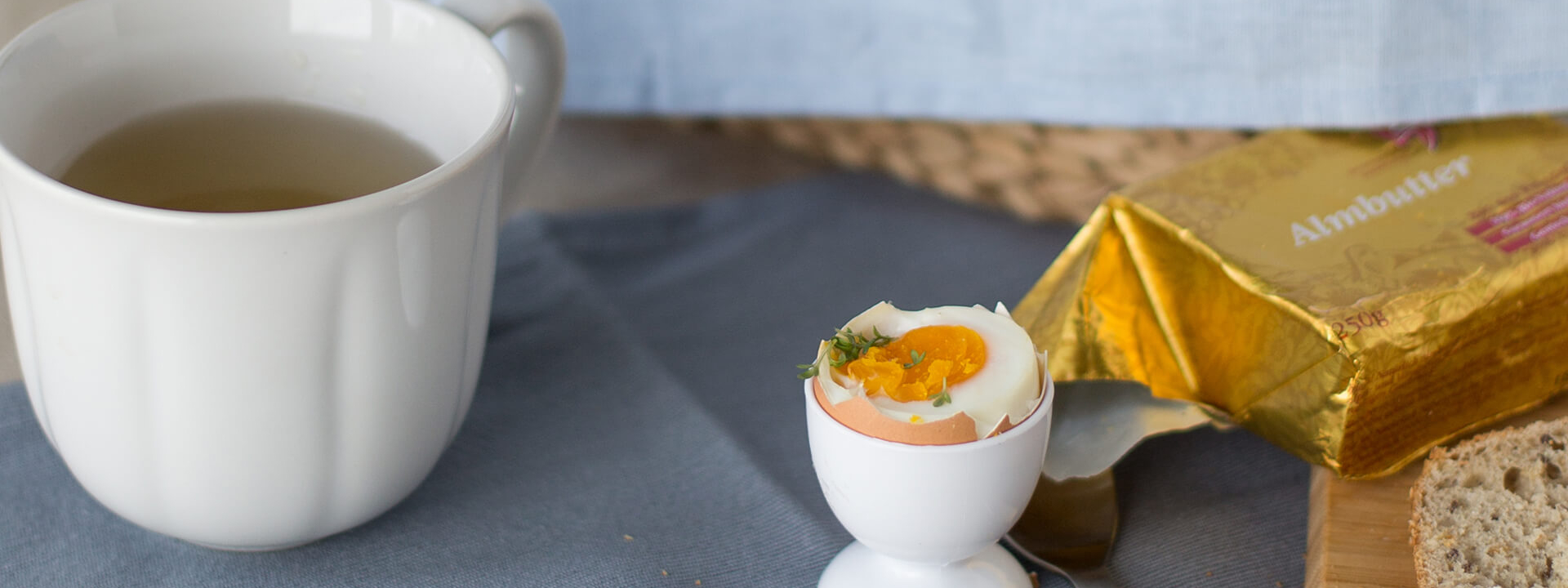 Ein gekochtes Bio-Ei mit Tee und Butter auf einem Tisch.