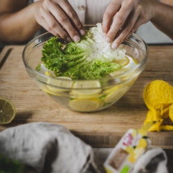 Jemand legt Ja! Natürlich Bio-Salat in eine Schüssel mit Wasser und Zitronen.