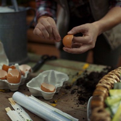 Jemand sticht mit einer Nadel ein Loch in den Boden einer halbierten Eierschale.