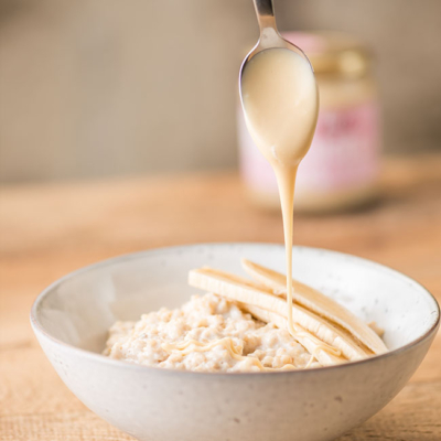 Jemand verteilt Bio-Mandelmus auf einer Schüssel mit Porridge.