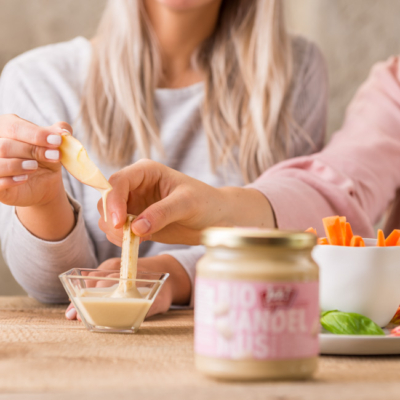 Jemand dippt in eine Schale mit Ja! Natürlich Bio-Mandelmus. Die Verpackung davon.