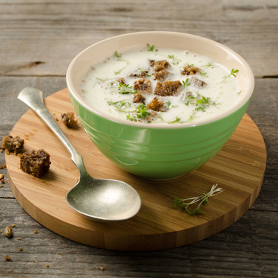 Eine Schüssel mit Bio-Bauernrahmsuppe, garniert mit Brotkrumen, auf einem runden Holztablett.