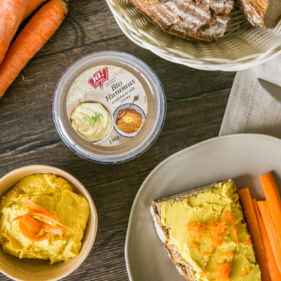 Nahaufnahme von einer Scheibe Brot und einer Packung Ja! Natürlich Bio-Hummus mit Curry.