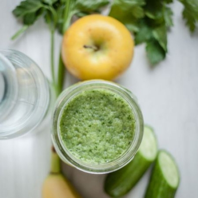 Grüner Smoothie mit Bio-Gurken und Äpfel am Tisch.