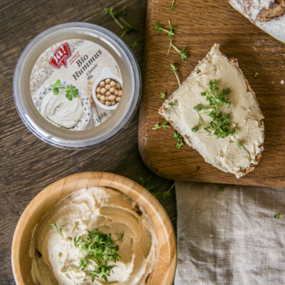 Nahaufnahme von einer halben Scheibe Brot und einer Packung Ja! Natürlich Bio-Hummus.