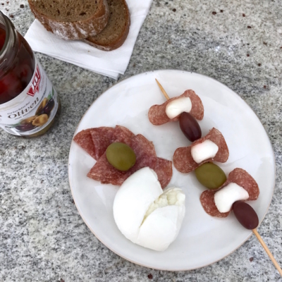 Auf einem Teller ist ein Spieß aus Ja! Natürlich Oliven, Bio-Mozzarella und Salami.