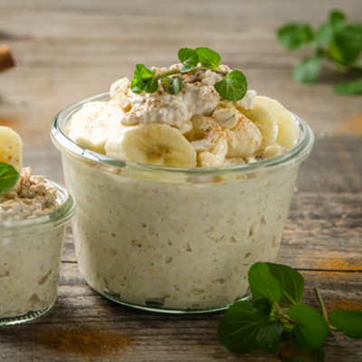 Zwei Gläser Nuss-Porridge mit Haferdrink und Bio-Bananen.