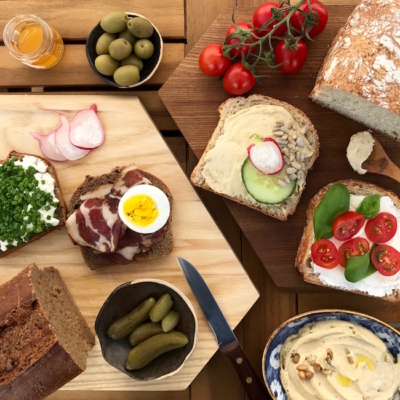 Mehrere Scheiben Bio-Brot, verschieden belegt mit Gemüse und Aufstrichen, daneben ein Messer.