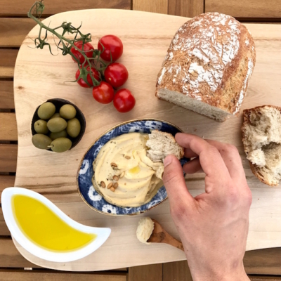 Jemand dipt mit einem Stück Brot in eine Schüssel mit Bio-Hummus.