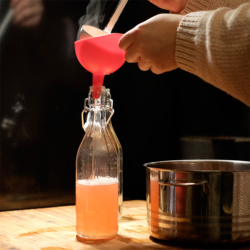 Jemand füllt Rhabarbersirup in eine Glasflasche.