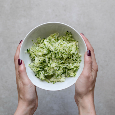 Jemand hält eine Schüssel gefüllt mit geraspelten Bio-Zucchini.