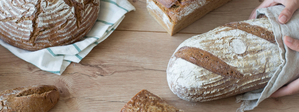 Jemand hält ein Laib Bio-Brot, daneben liegen noch diverse Brotsorten.