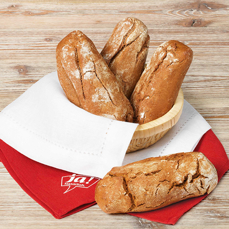 Ein Korb mit drei Laiben Bio-Brot, und ein Laib liegt neben dem Korb.