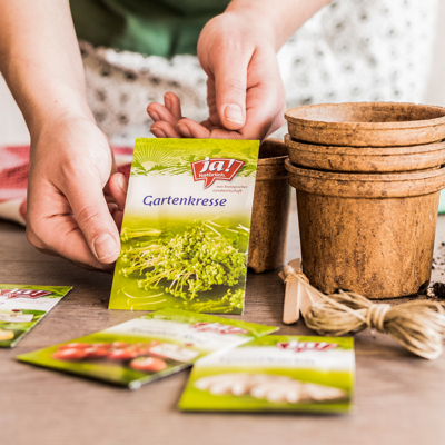 Jemand hält eine Packung Ja! Natürlich Bio-Gartenkresse-Samen.