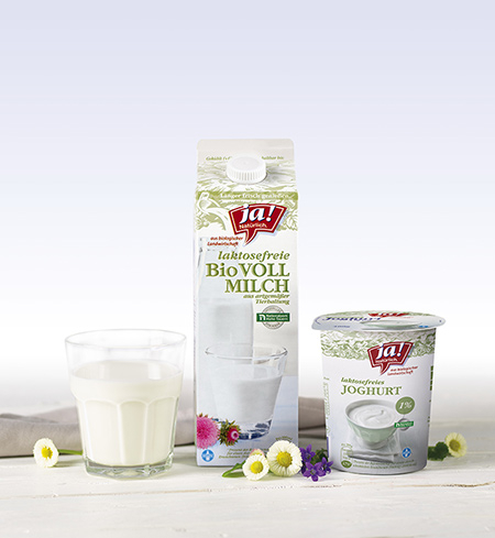 Ein Karton Ja! Natürlich Bio-Vollmilch neben einem Glas Milch und Joghurt.