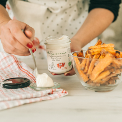 Jemand gibt einen Löffel voll Ja! Natürlich Bio-Mayonaise neben eine Schüssel mit Süßkartoffeln