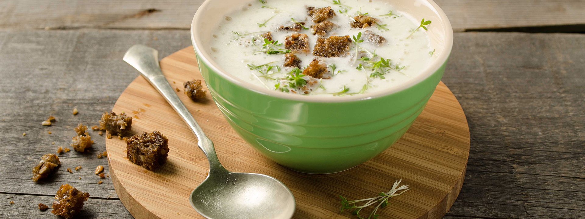 Eine Schüssel mit Bio-Bauernrahmsuppe, garniert mit Brotkrumen, auf einem runden Holztablett.