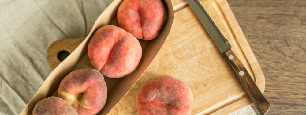 Bio-Plattpfirsiche auf einem Schneidebrett mit einem Messer.