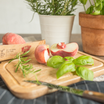 Aufgeschnittener Bio-Plattpfirsich mit einem Messer und Kräutern.