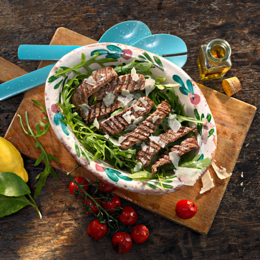 Eine ovale Schüssel mit Bio-Rucola, auf der dünn angebratene Steakstreifen liegen.