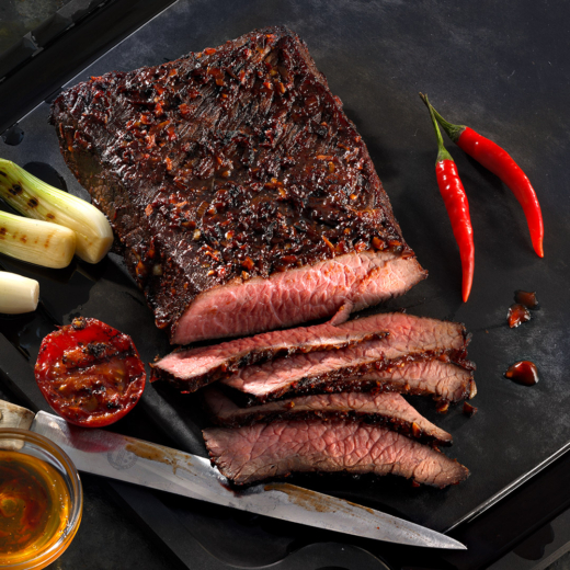 Ein Bio-Roastbeef im Ganzen auf einem Brett mit Chilischoten und Paradeisern.